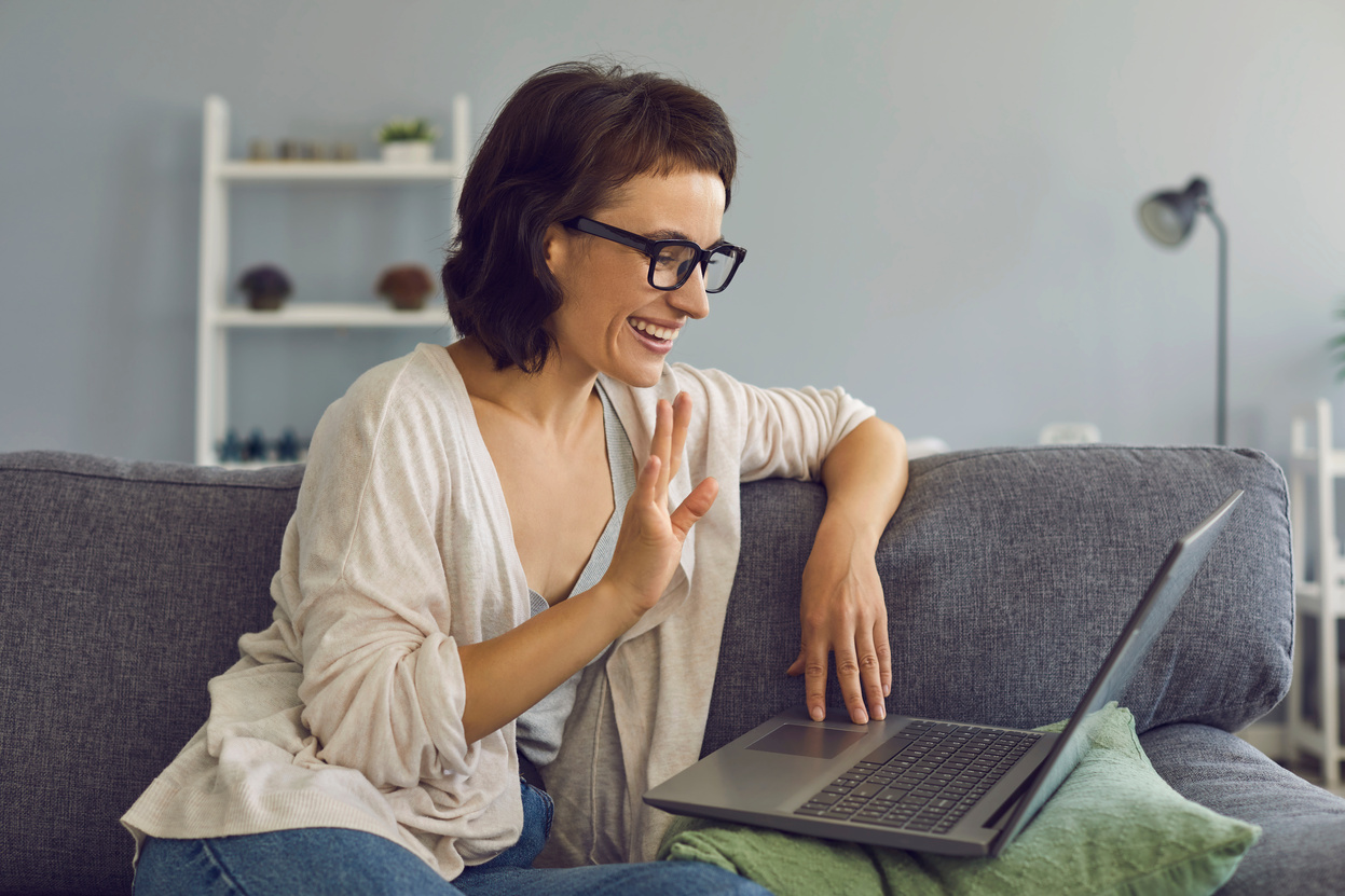 Smiling Woman Greeting Somebody during Online Conversation on Laptop at Home